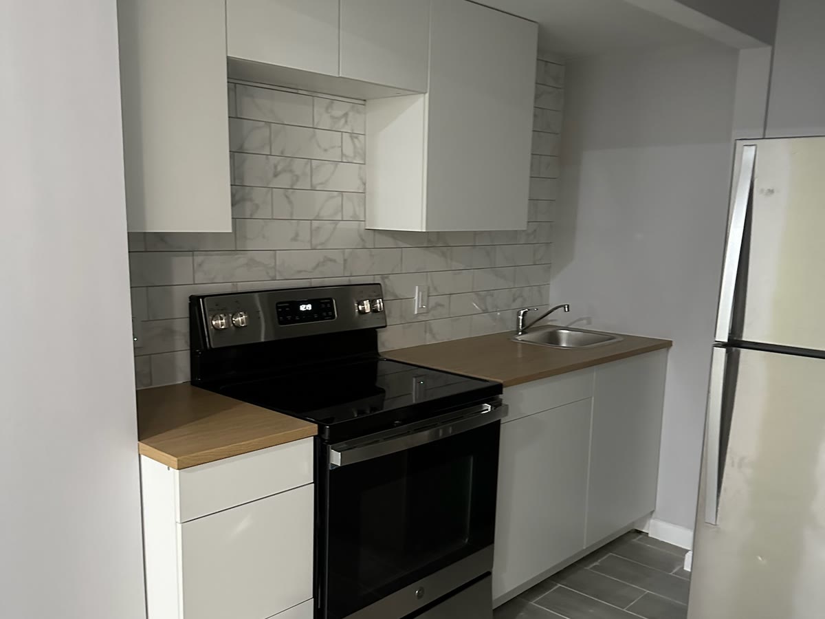 Real ARCED basement apartment — kitchenette with flat-panel cabinets, marble subway backsplash, butcher-block counters