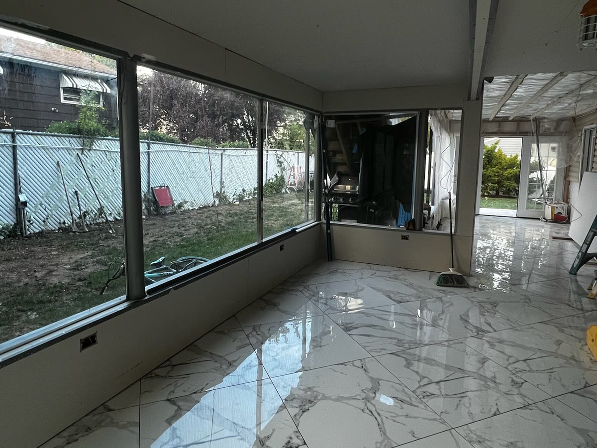 Real ARCED apartment addition — enclosed sunroom living space with glass walls and marble-look tile floor